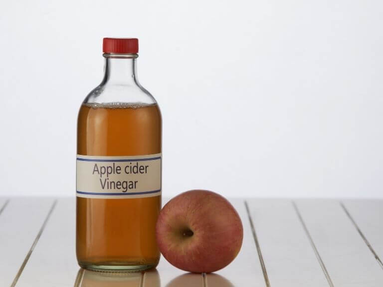 a bottle a apple cider vinegar next to an apple