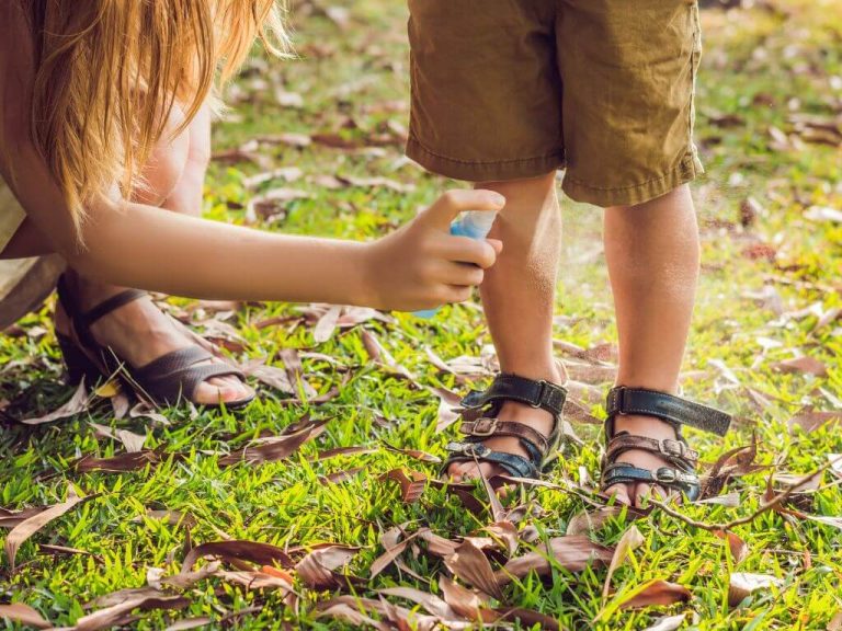an adult spraying repellent on a kid's legs
